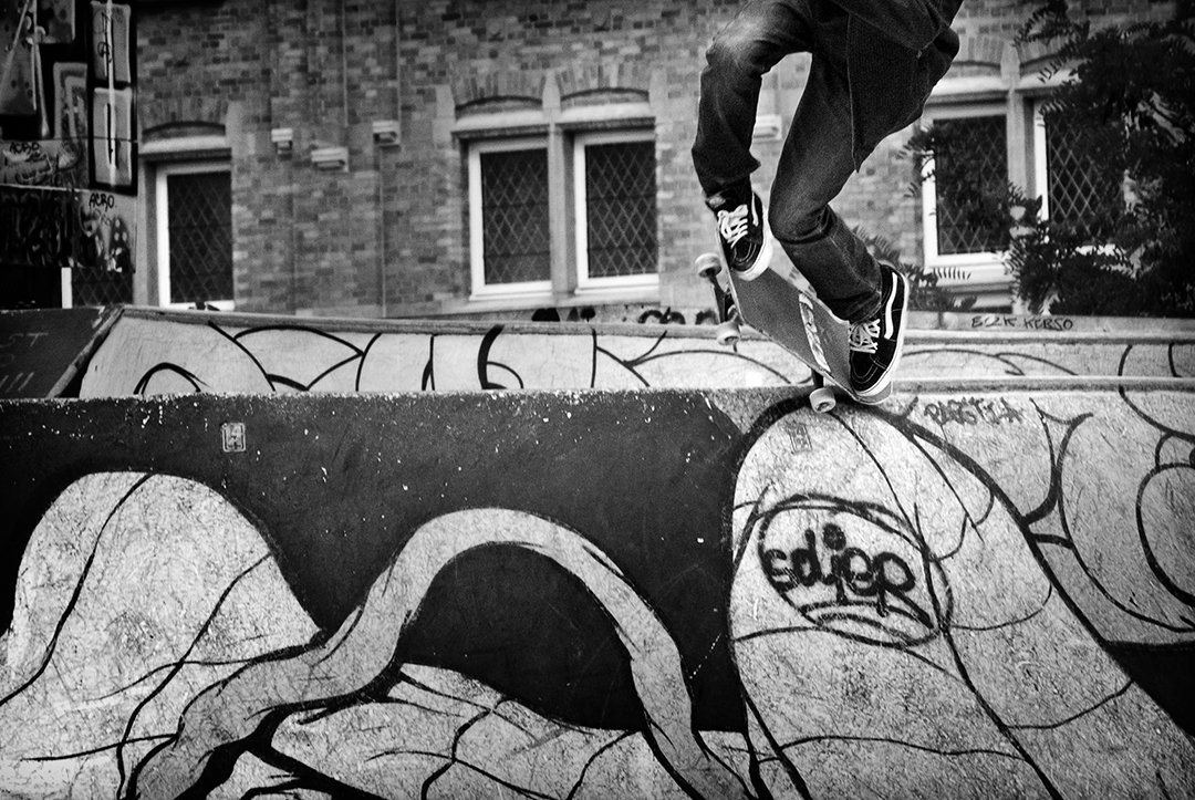 A person jumping over a wall with graffiti, seen at foot level.